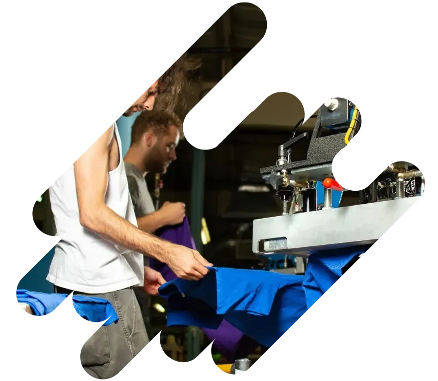 Two workers printing blue T-shirts in a garment production facility, showcasing the behind-the-scenes process of custom apparel manufacturing.